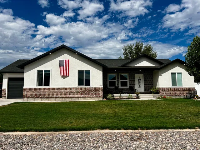 Contemporary ranch-style facade featuring a dark asphalt shingle roof, light stucco, and a brick skirt