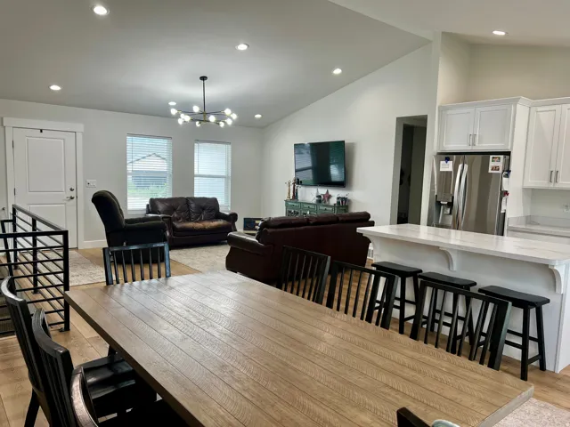 Open-concept living space featuring vaulted ceilings, recessed lighting, wood-finish flooring, a kitchen island with seating, and white cabinetry