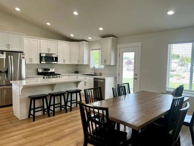 Kitchen and dining area featuring white cabinetry, light-toned countertops, stainless steel appliances, wood-finish flooring, and recessed lighting