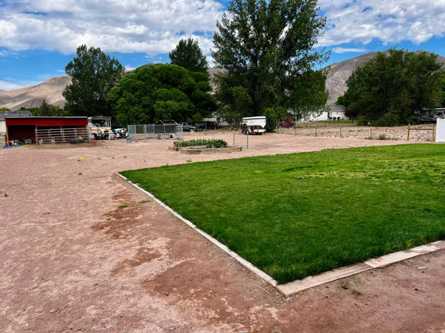 Expansive outdoor space featuring a manicured lawn, established perimeter trees, and a mountain backdrop