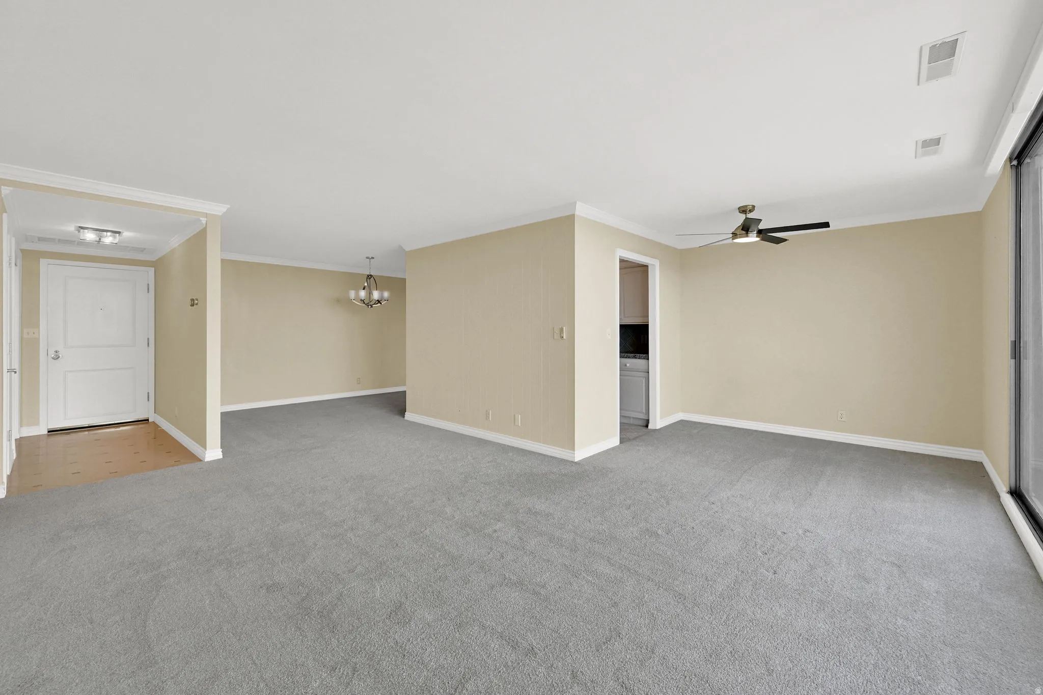 Spacious living area with neutral carpet flooring, a ceiling fan, and sliding glass door