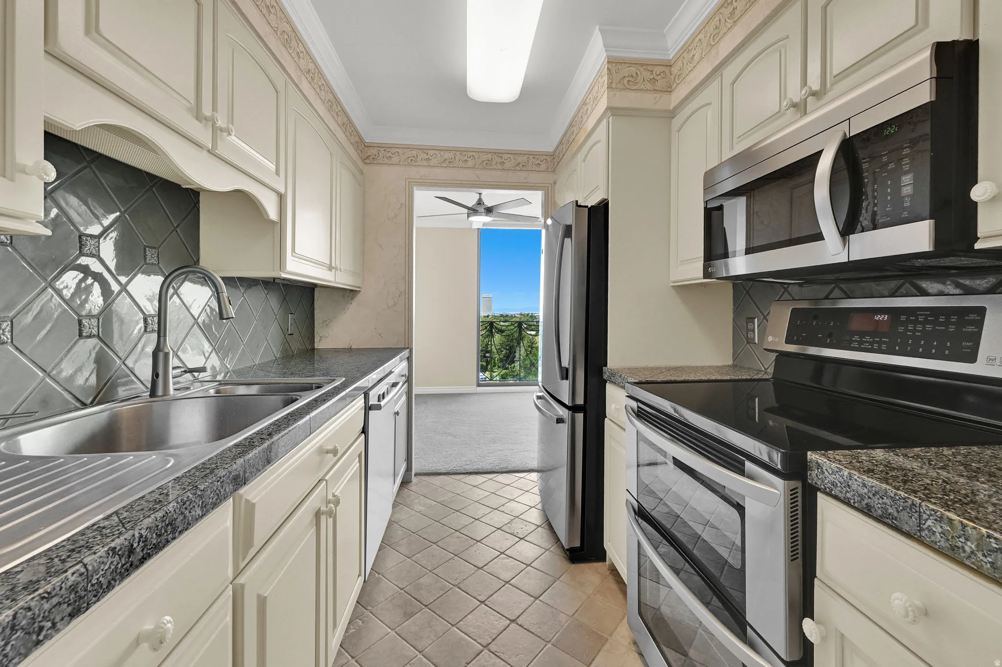 Kitchen featuring light-toned cabinetry, stainless steel appliances, a double basin sink, patterned tile backsplash, and stone-finish countertops