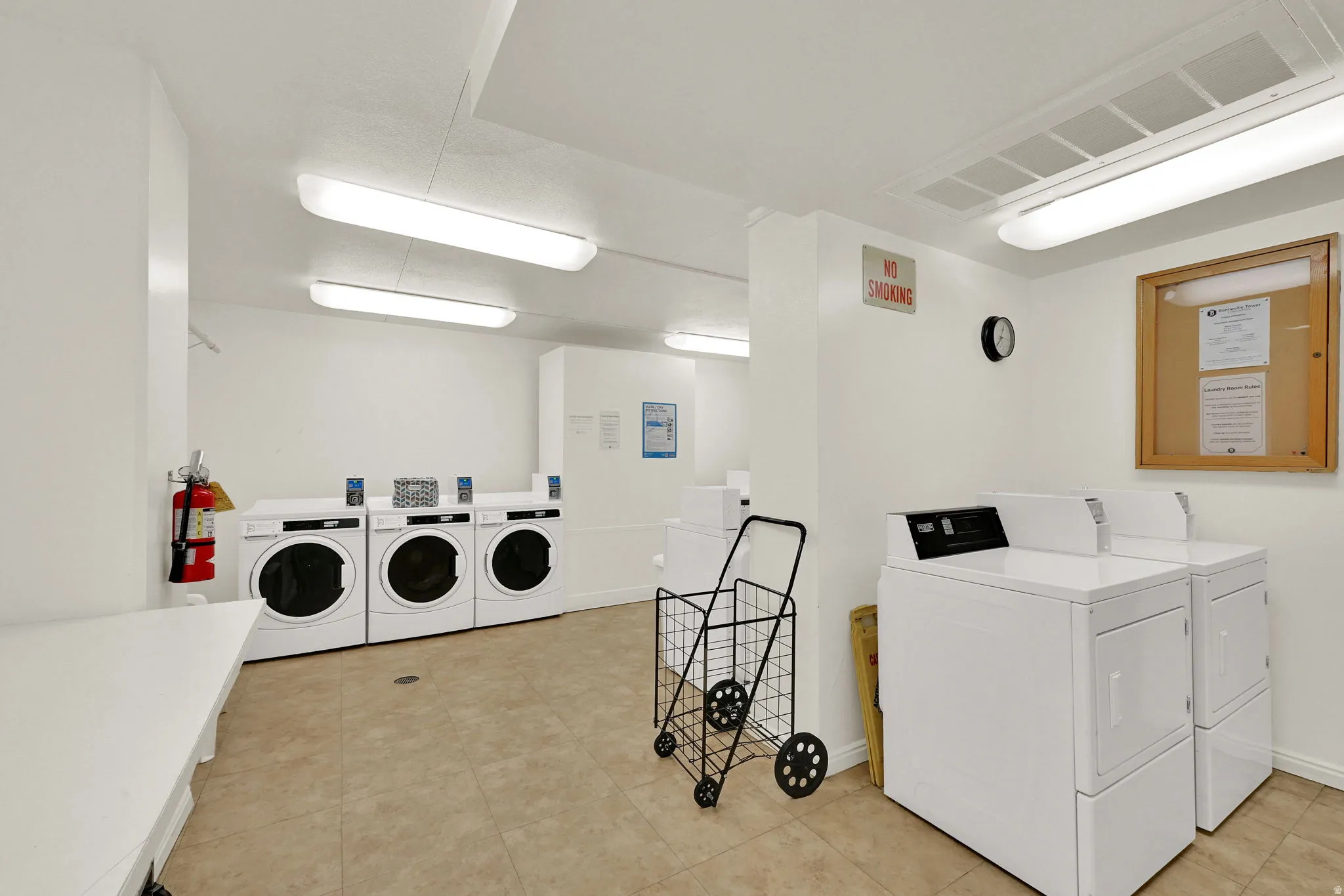 On-site laundry facility featuring multiple front-loading and top-loading machines, fluorescent ceiling lighting, and tiled flooring