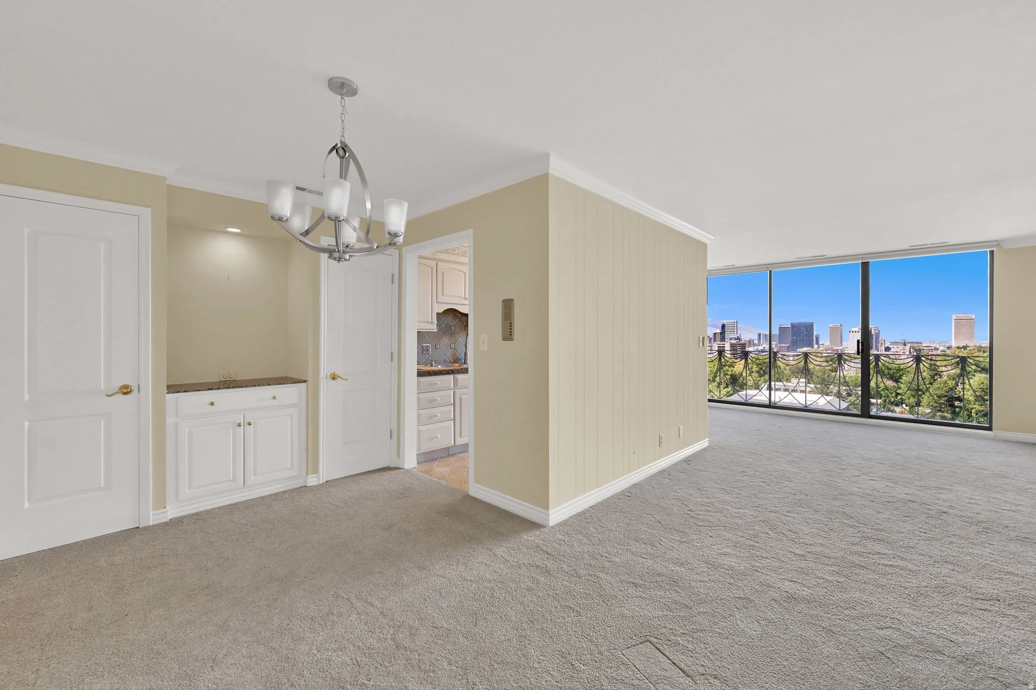 Floor-to-ceiling windows, city skyline, built-in cabinetry with stone countertop, suspended light fixture, and crown molding
