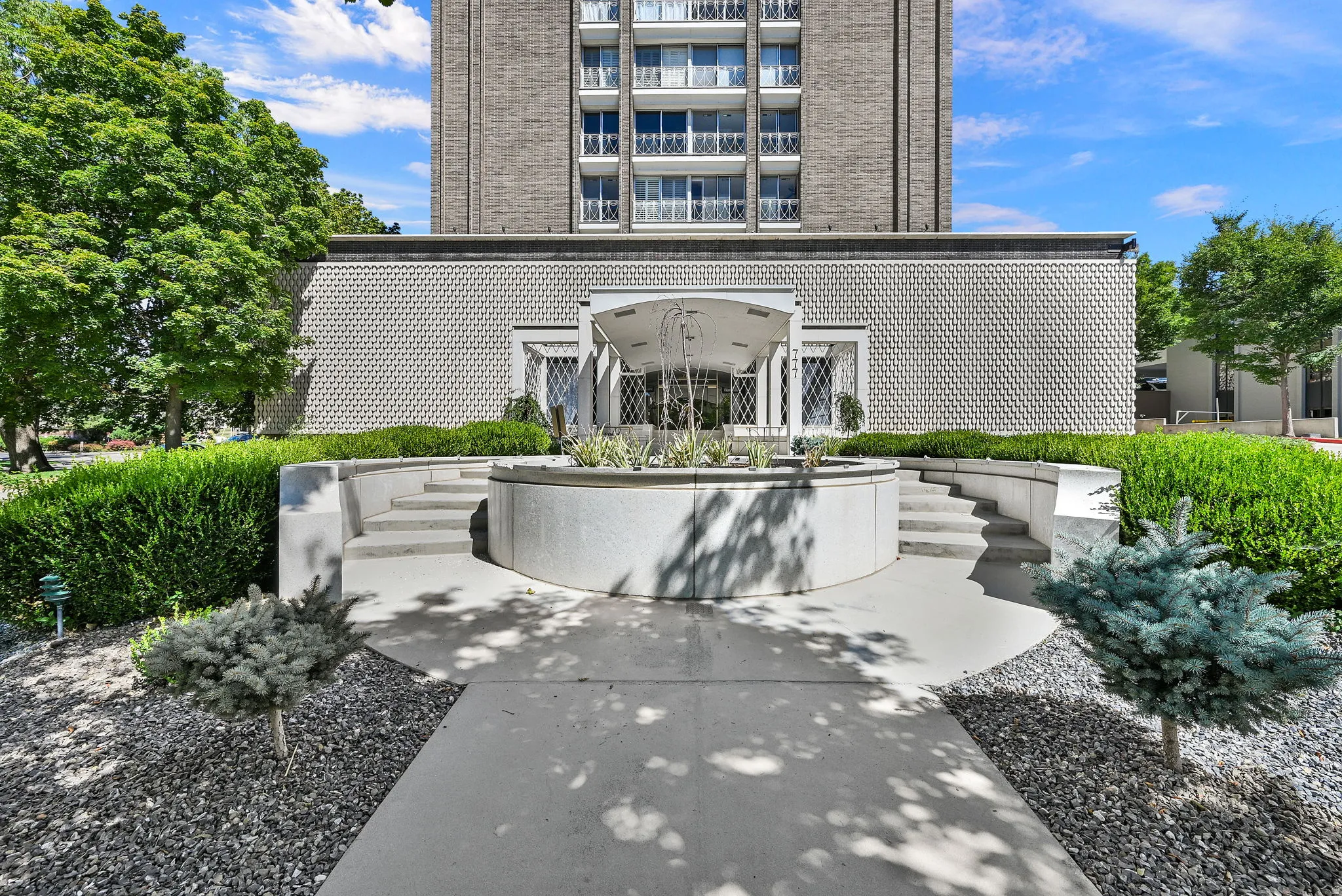 Architectural entrance featuring a circular concrete planter, curved concrete stairs, and a metal portico