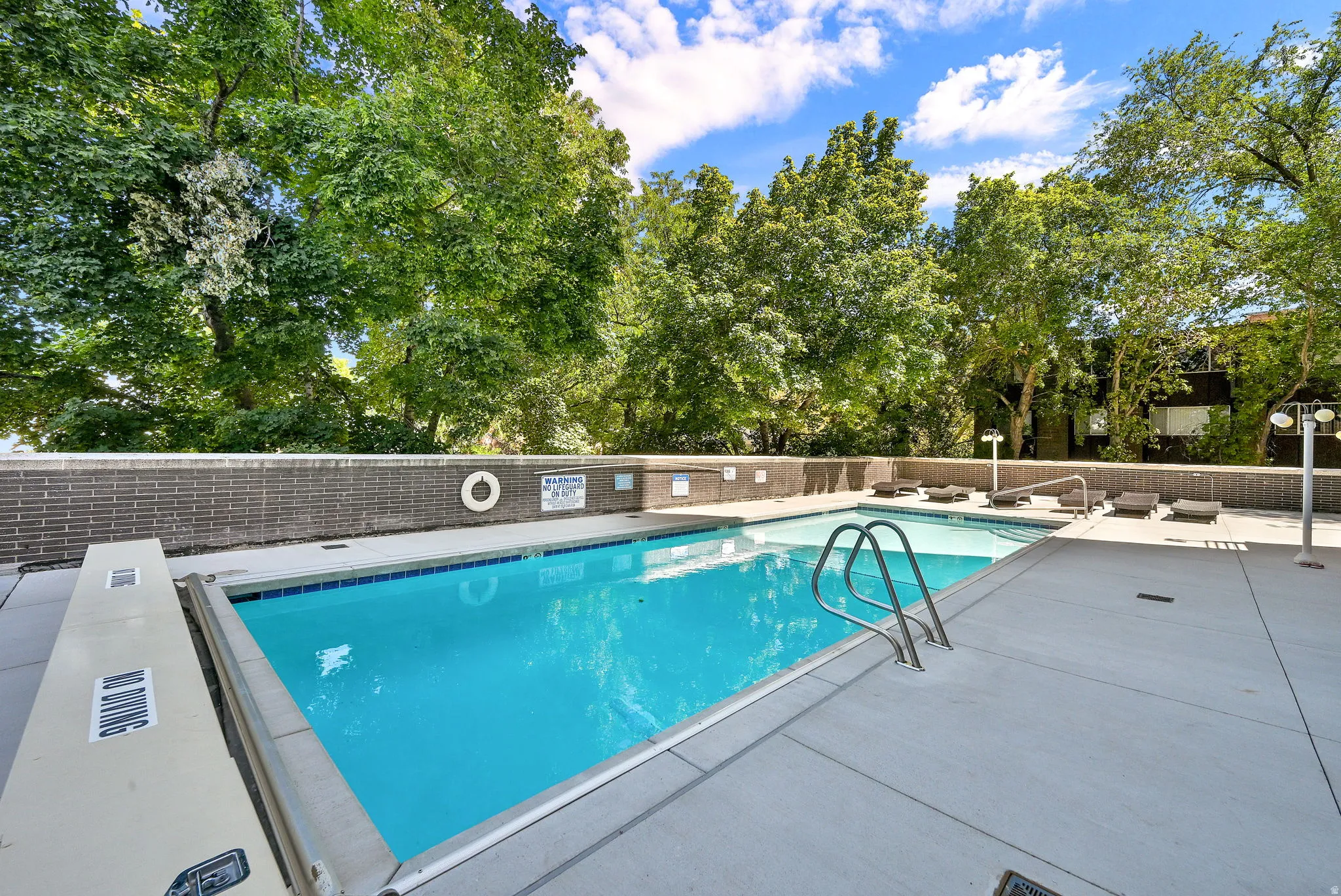 Outdoor swimming pool with integrated steps, surrounded by a concrete deck, and a brick-finish retaining wall