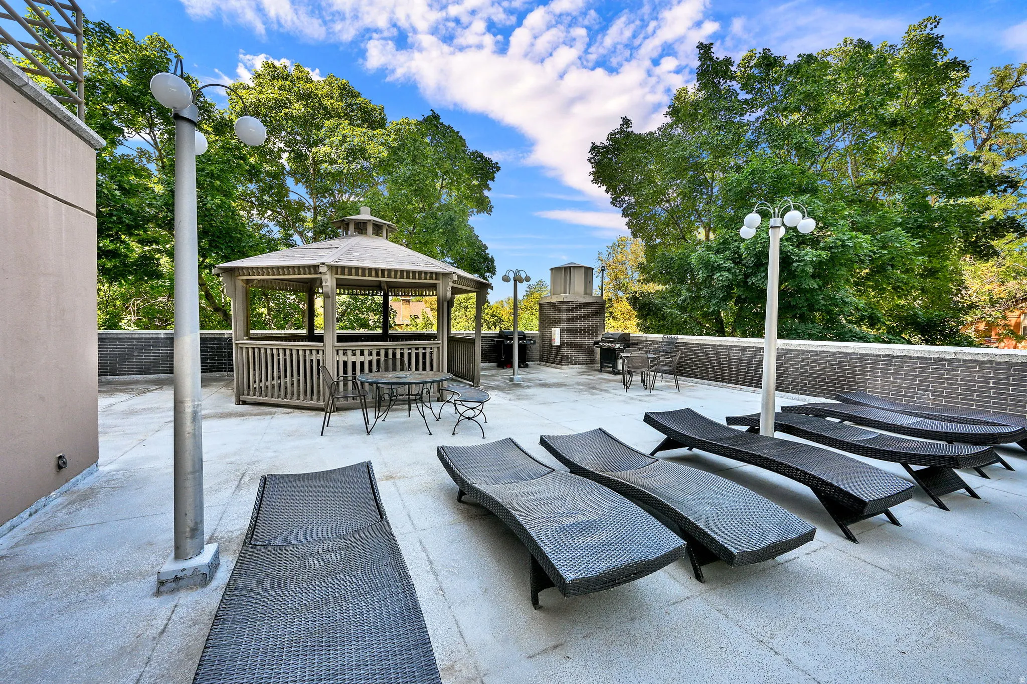 Rooftop patio featuring a gazebo, integrated grilling station, concrete flooring, and perimeter brick wall