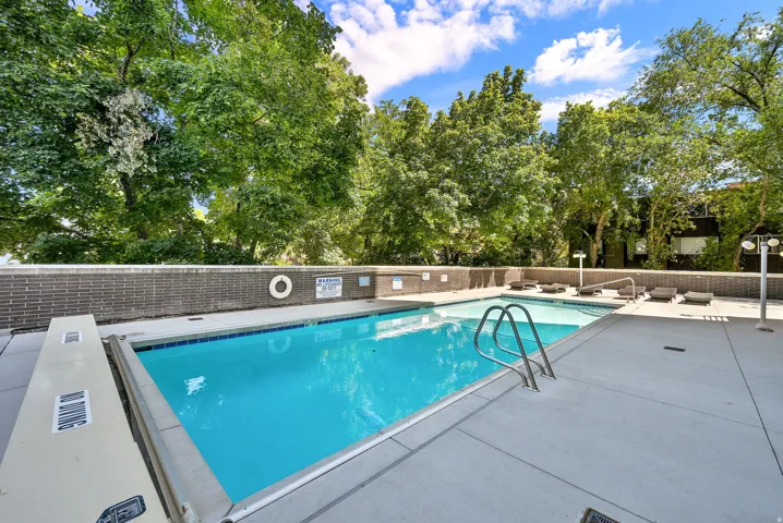 Outdoor swimming pool with integrated steps, surrounded by a concrete deck, and a brick-finish retaining wall