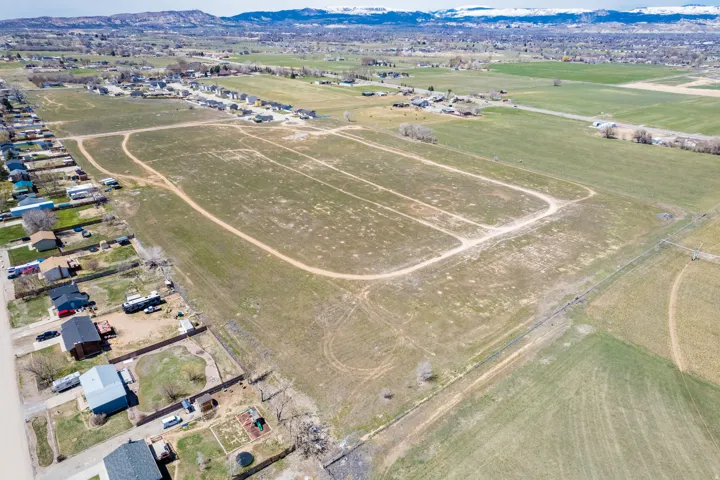 Expansive land parcel featuring existing residential properties, adjacent open fields, and distant mountain ranges