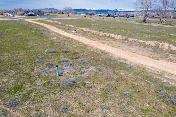 Expansive undeveloped land with a dirt access path and visible utility infrastructure, complemented by distant mountain scenery