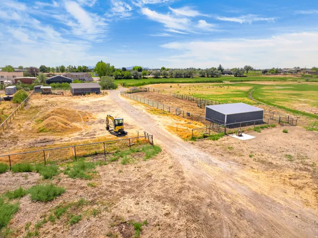 Gravel drive with metal fencing, open land, and multiple outbuildings