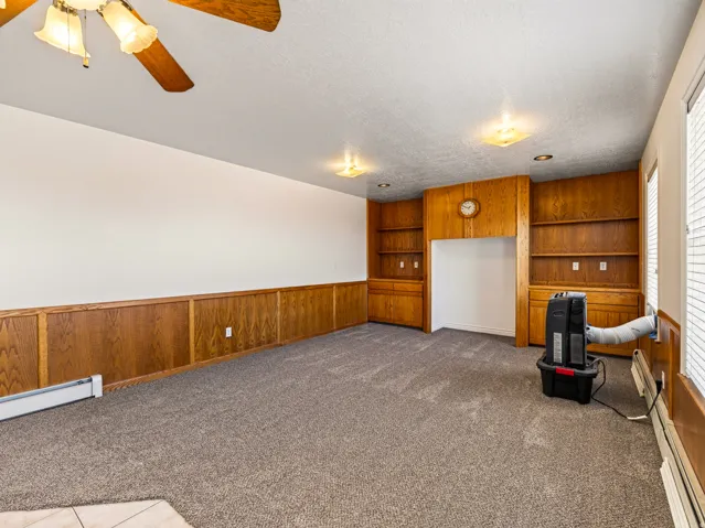 Wall-to-wall carpeting, wood-paneled walls, built-in shelving, ceiling fan with light fixture, and recessed lighting