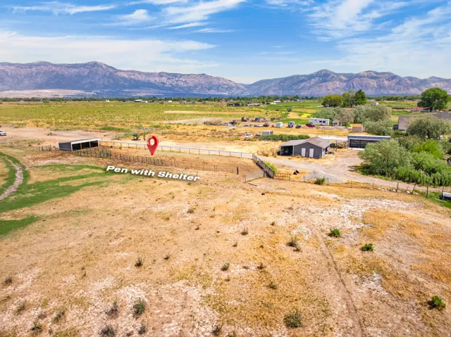 Expansive rural property featuring a fenced pen with an integrated shelter, additional outbuildings, and distant mountain scenery