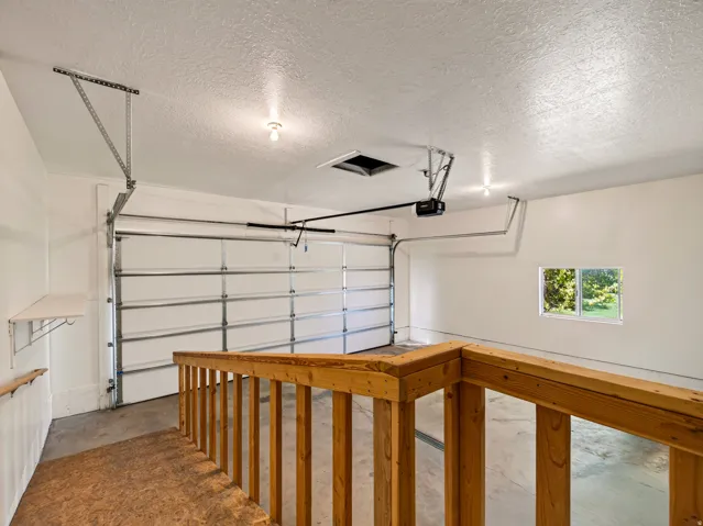Overhead garage door with automatic opener, concrete flooring, wooden handrail, built-in shelving, and a window