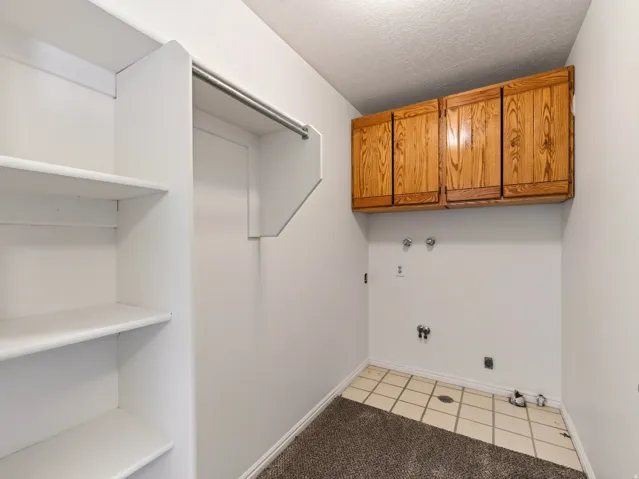 Built-in shelving, hanging rod, wood-finish cabinetry, utility hook-ups, and square tile flooring