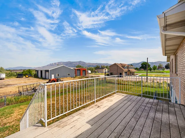 Exterior balcony featuring wood-finish decking, white metal railing, and brick siding