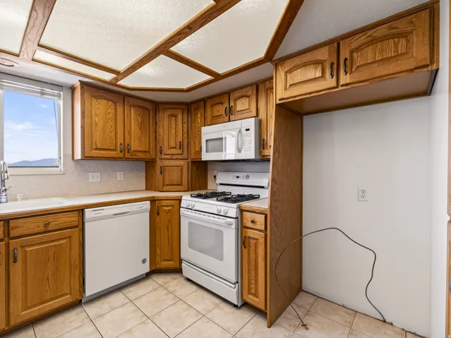 Kitchen featuring wood-finish cabinetry, tile flooring, white appliances, and a window with blinds