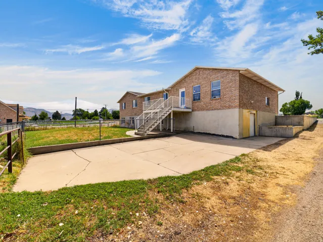 Brick-finish exterior with multiple windows, concrete patio, and exterior staircase access