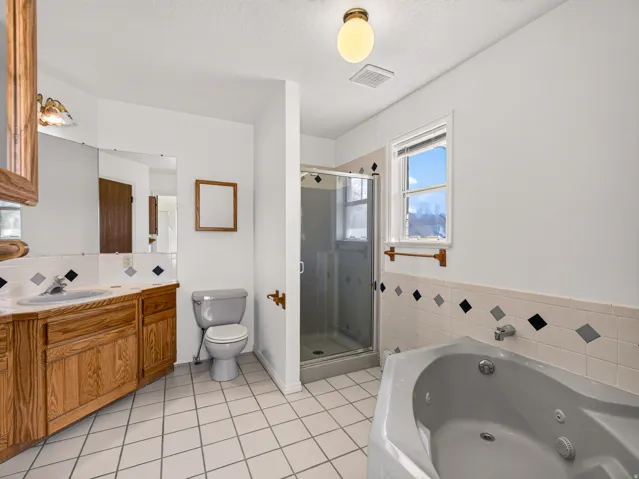 Corner bathtub, glass-enclosed shower, wood vanity with integrated sink, tiled flooring, and accent wall tiling