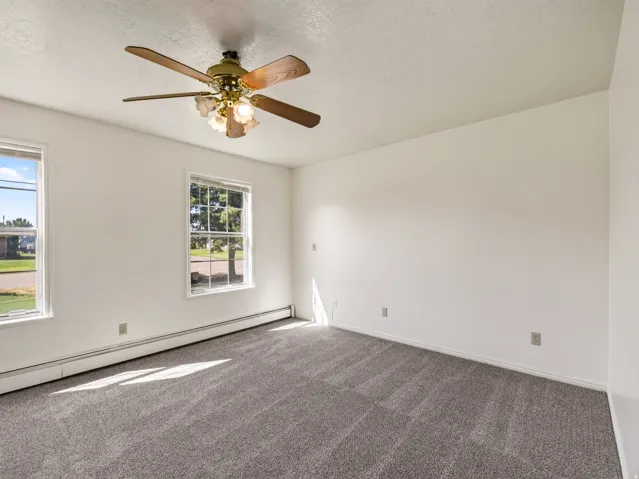 Spacious room featuring neutral carpeting, white walls, two windows, and a ceiling fan with integrated lighting