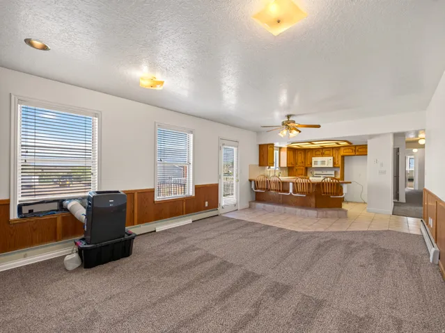 Open-concept layout with carpeted living space and tiled kitchen, featuring wood-finish cabinetry, white appliances, and a ceiling fan