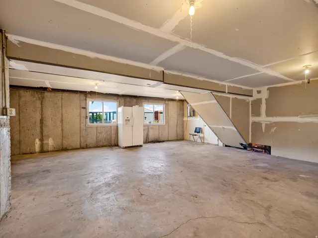 Concrete flooring, exposed concrete walls, two windows, partial drywall installation, and exposed ceiling joists