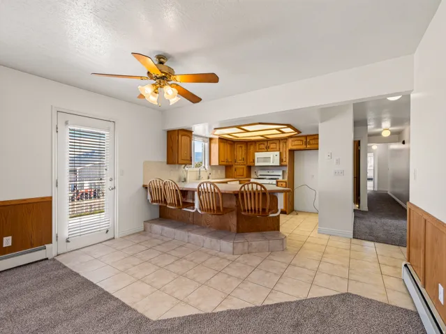 Kitchen with wood cabinetry, white appliances, and a tiled breakfast bar with seating