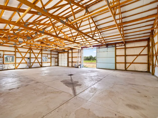 Expansive interior featuring an exposed wood beam ceiling, concrete flooring, multiple overhead lighting fixtures, and large sliding doors