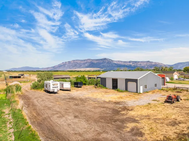 Metal-sided barn structure with multiple garage doors, a gravel driveway, and a partially fenced perimeter