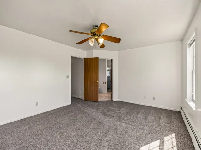 Spacious room featuring neutral carpeting, a ceiling fan with integrated lighting, and multiple windows