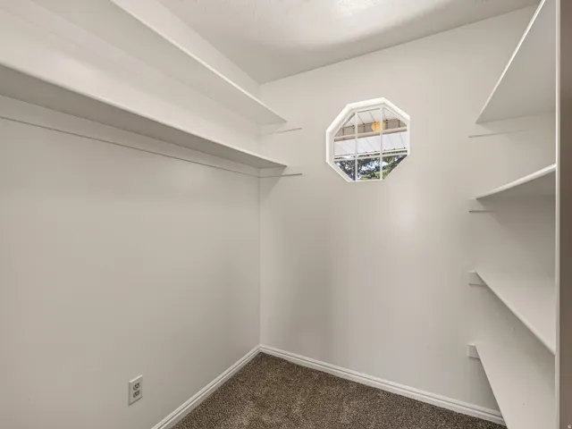 Built-in shelving, octagonal window, white interior walls, and carpeted flooring