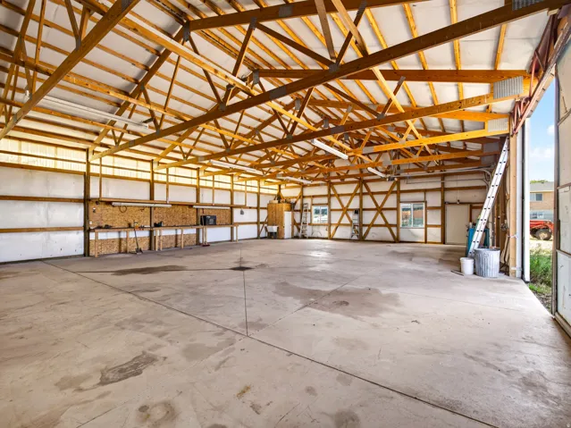 Spacious interior with exposed wood beam trusses, concrete flooring, and a large roll-up door