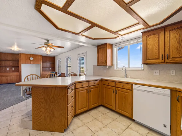 Kitchen area featuring wood cabinetry, a built-in dishwasher, and a sink with a window above