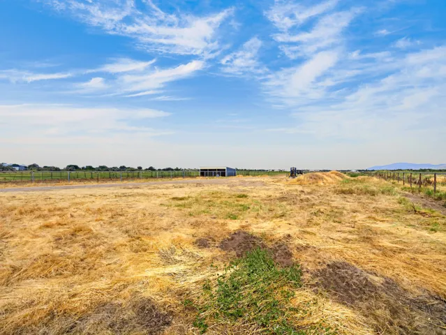 Expansive undeveloped land with a distant blue outbuilding and partially visible fencing