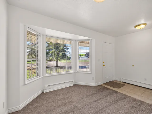 Bay window with blinds, carpeted flooring, tiled entry, panel door, and flush-mount lighting fixtures
