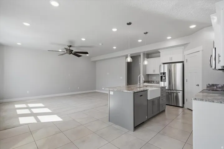 Recessed lighting, ceiling fan, tile flooring, kitchen island with sink, and stainless steel refrigerator