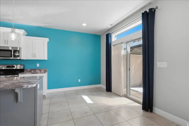 White cabinetry, stainless steel appliances, granite-look countertops, tiled flooring, and a sliding glass door