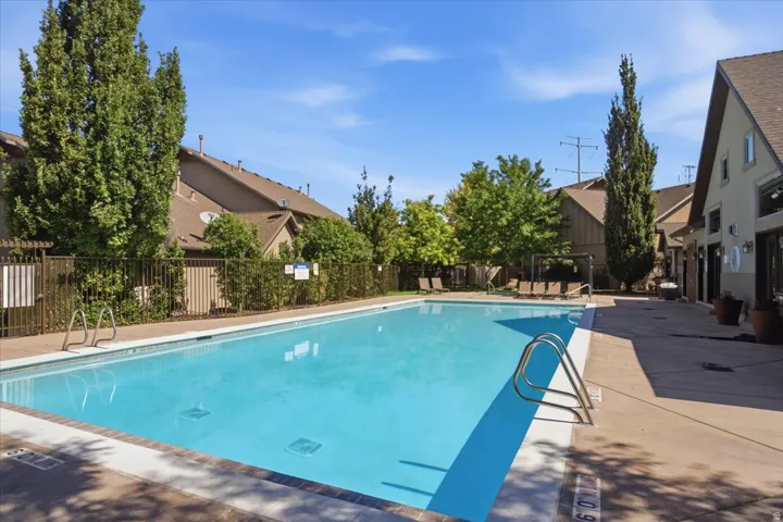 Outdoor swimming pool with integrated steps, surrounded by a concrete deck and mature landscaping, and bordered by a metal fence