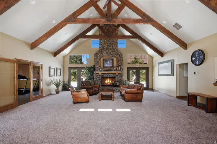 HOA Clubhouse Vaulted ceiling with exposed wood beams, stone-clad fireplace, built-in fireplace mantel, and glass-paneled double doors