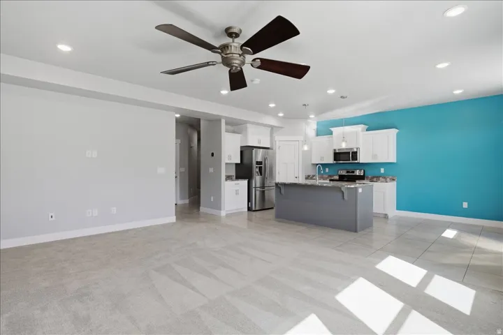 Recessed lighting, ceiling fan, kitchen island with sink, stainless steel appliances, and white cabinetry
