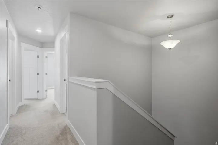Recessed ceiling lighting, durable carpeting, interior doors with panel detailing, painted handrail, and a hanging pendant light fixture