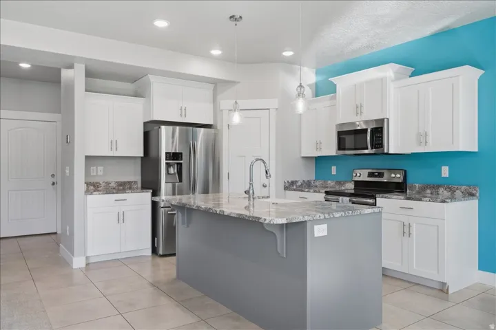 Kitchen featuring white cabinetry, stainless steel appliances, a center island with sink, and tile flooring