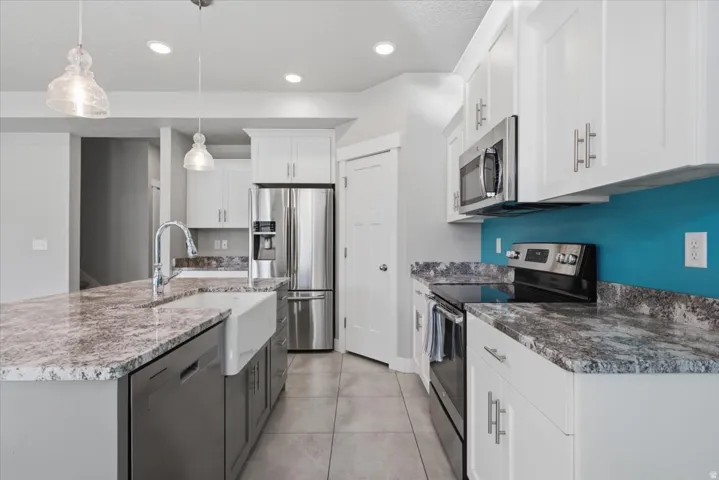 Kitchen featuring white cabinetry, gray and white countertops, a farmhouse sink, stainless steel appliances, and tile flooring