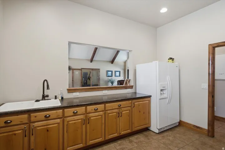 HOA Clubhouse Kitchen Spacious utility area featuring wood-finish cabinetry, a large single-basin sink with a gooseneck faucet, dark countertops, and tiled flooring