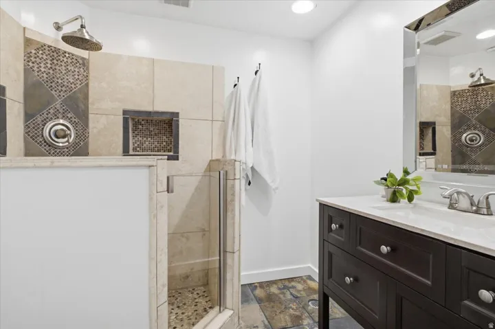 Updated bathroom featuring a walk-in shower with rain showerhead, mosaic tile accents, and a built-in storage cabinet.