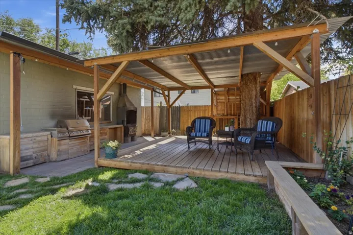 Expansive covered wood deck designed for outdoor entertaining, featuring an aluminum roof covering, built-in outdoor kitchen with grill, stone paver pathway, and wood privacy fencing.