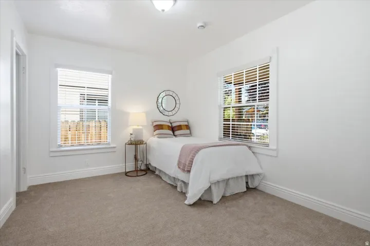 Comfortable second bedroom on the main floor featuring plush carpet flooring, white painted walls, and window blinds for privacy and natural light control.
