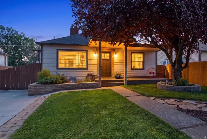 Siding exterior featuring a covered front porch entry, mature landscaping, and a paver-lined driveway.