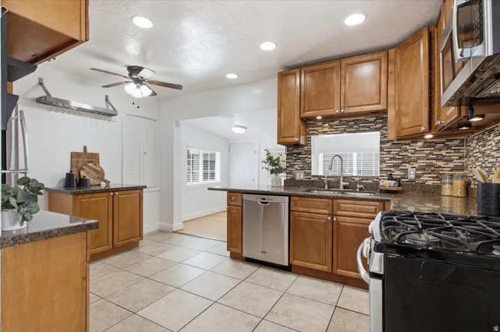 Well-appointed kitchen featuring recessed lighting, tiled backsplash, granite countertop, wood cabinetry, stainless steel dishwasher, and ceiling fan.