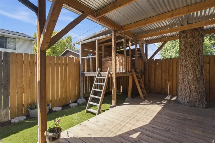 Outdoor living area featuring a covered wood deck patio, corrugated metal roof, wood privacy fencing and a built-in play area.